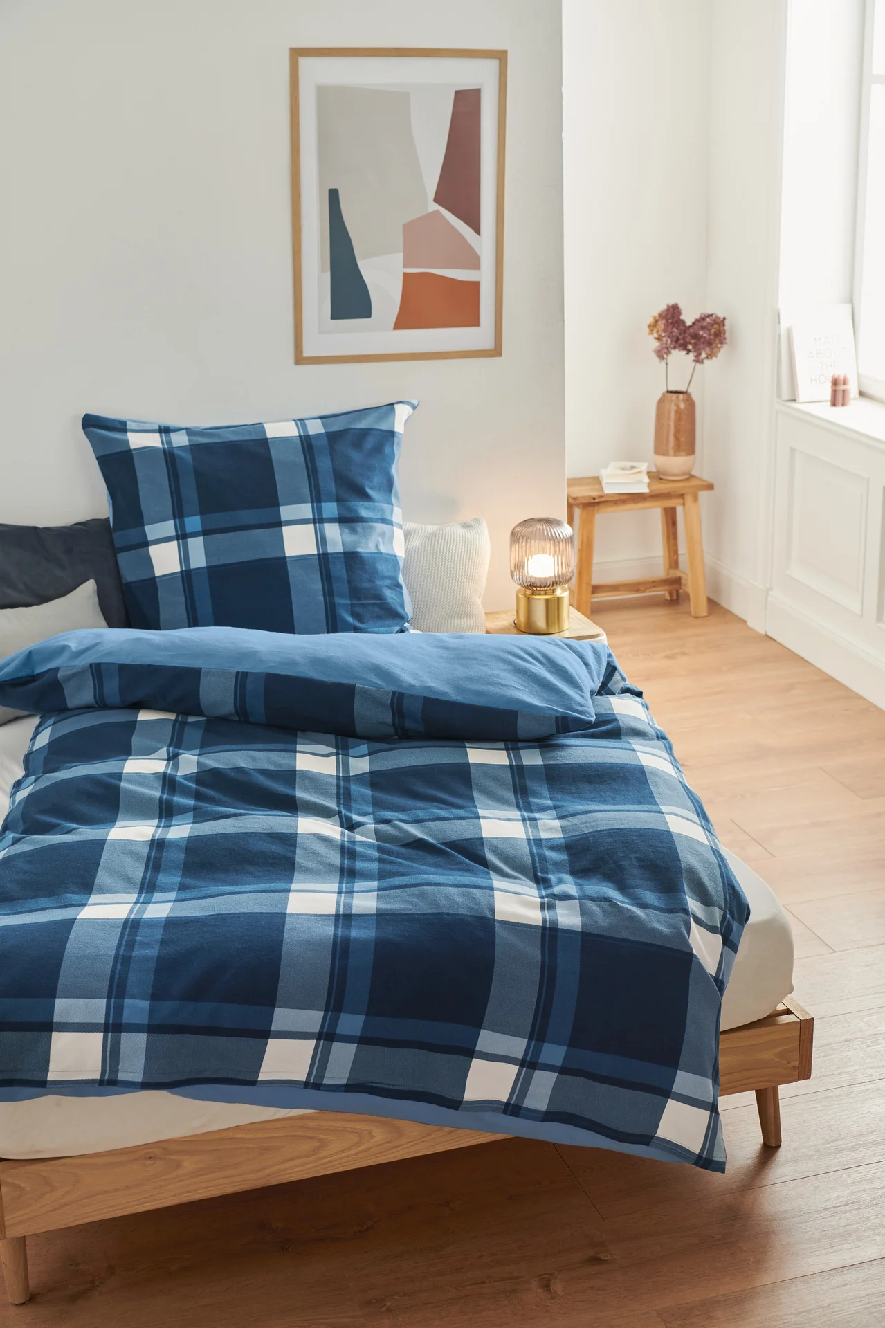 Auf einem Bett liegt Biber-Bettwäsche mit blauem Karomuster.
