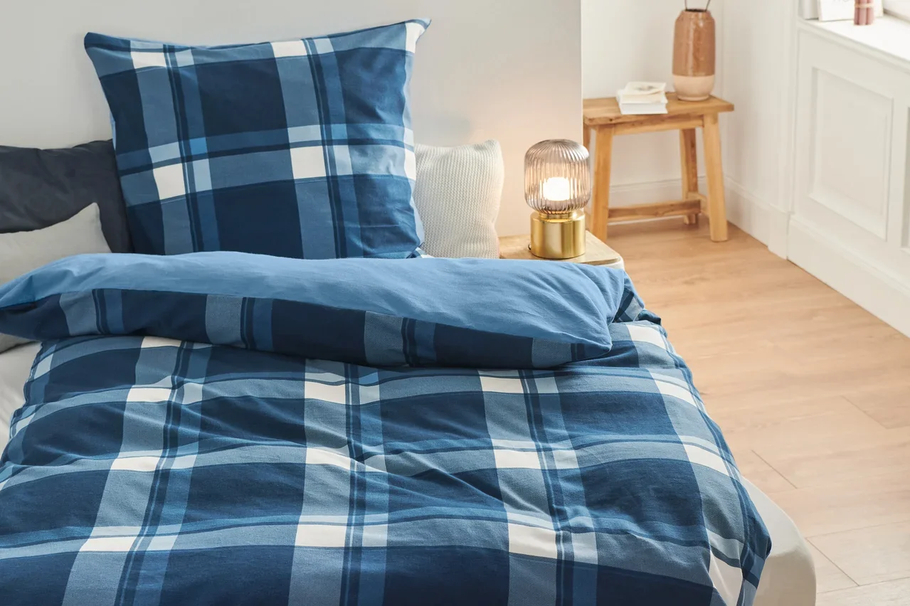 Auf einem Bett liegt Biber-Bettwäsche mit blauem Karomuster.
