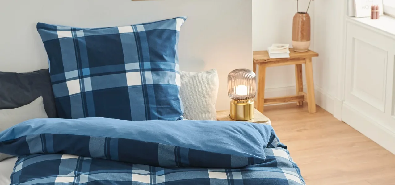 Auf einem Bett liegt Biber-Bettwäsche mit blauem Karomuster.
