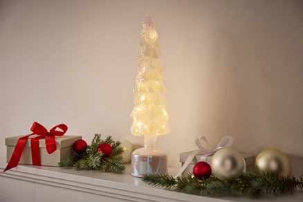 Ein dekorativer, beleuchteter Baum steht zwischen Geschenken und Ornamenten.