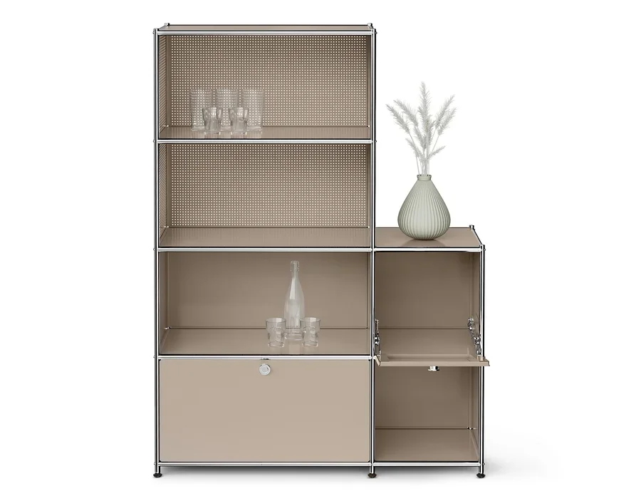 Ein beiges modulares Regal mit Chromrahmen. Die oberen linken Fächer haben perforierte Rückwände, das oberste Fach enthält klare Gläser. Das mittlere linke Fach enthält eine klare Flasche und zwei Gläser. Unten links befindet sich ein geschlossener Schrank. Das obere rechte Fach hat eine hellgrüne Vase mit weißen Zierpflanzen. Unten rechts ist ein offener Schrank mit einer Klapptür.