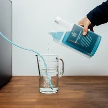 Person gießt flüssigen Reiniger in ein Glas, ein Schlauch führt zum Kaffeevollautomaten.