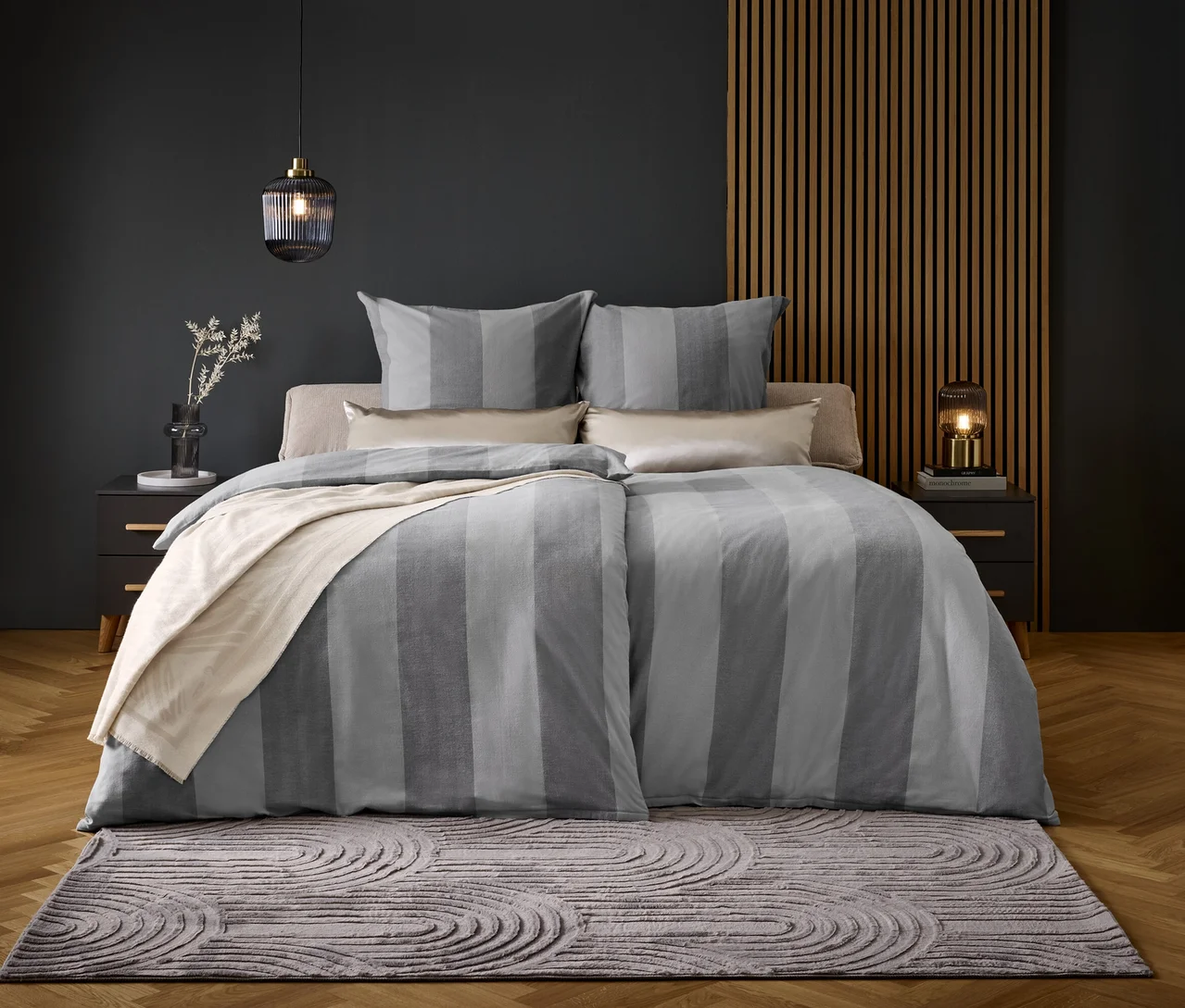 Ein Bett mit grau gestreifter Bettwäsche und Kissen auf einem grauen Teppich.