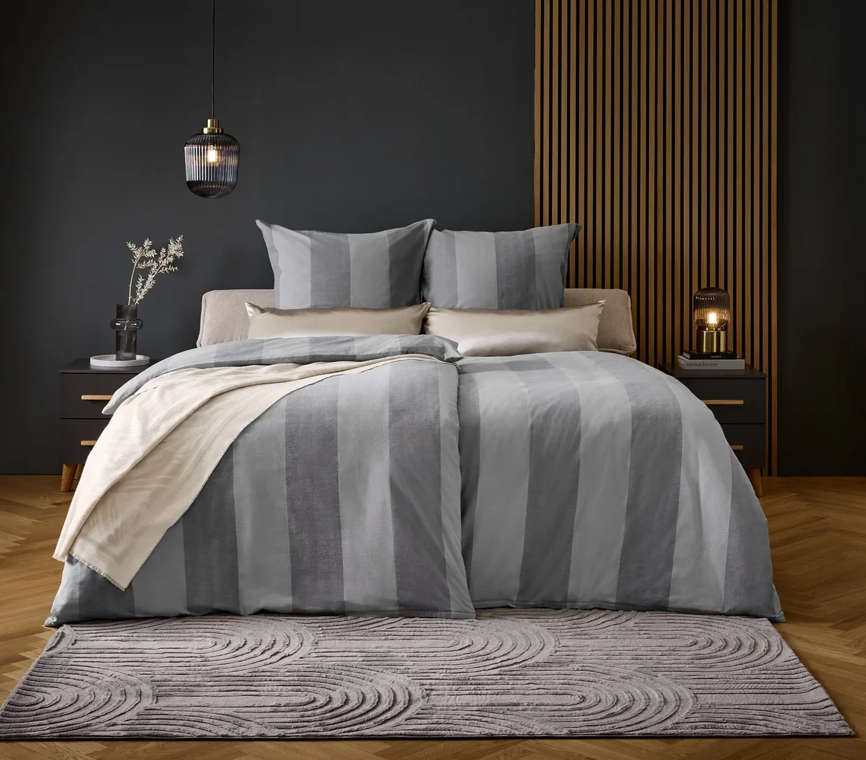 Ein Bett mit grau gestreifter Bettwäsche und Kissen auf einem grauen Teppich.