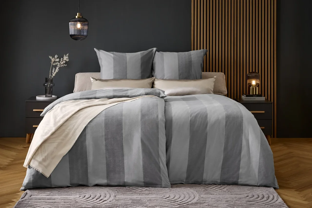 Ein Bett mit grau gestreifter Bettwäsche und Kissen auf einem grauen Teppich.
