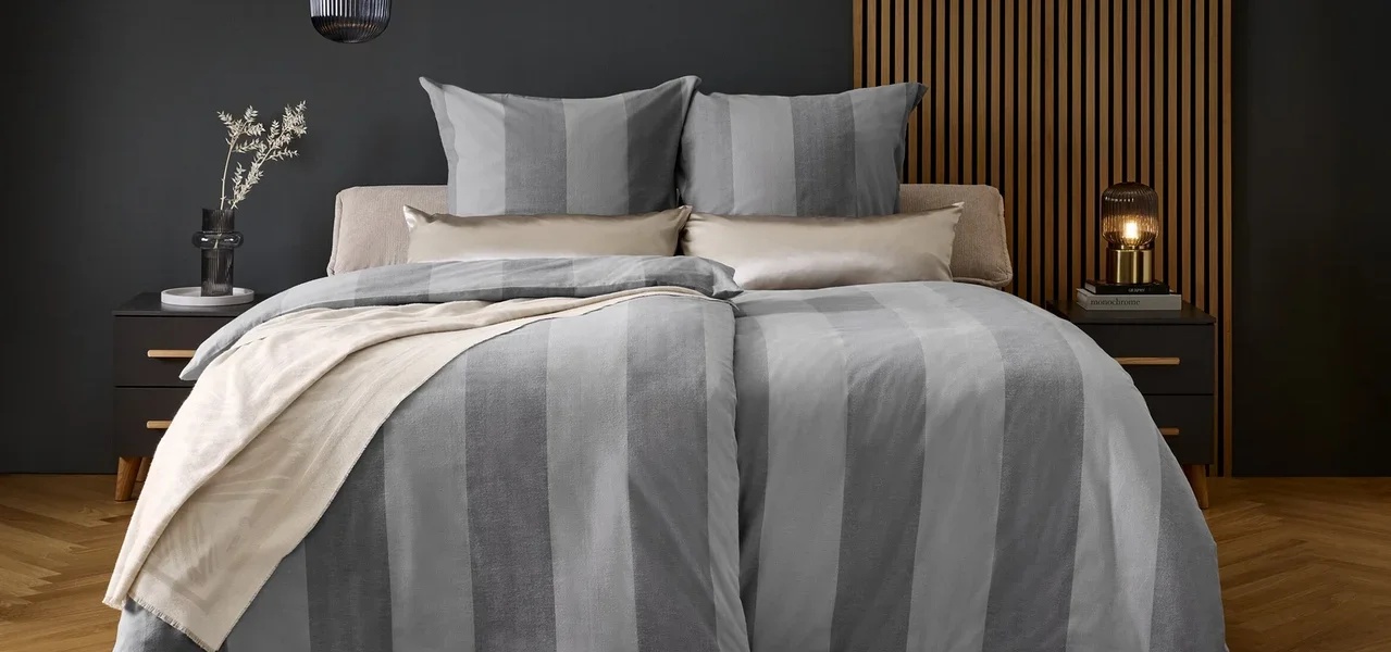 Ein Bett mit grau gestreifter Bettwäsche und Kissen auf einem grauen Teppich.