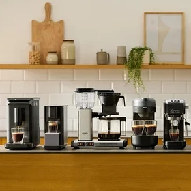 Verschiedene Kaffeemaschinen stehen auf einer Küchentheke vor einer weißen Fliesenkulisse.