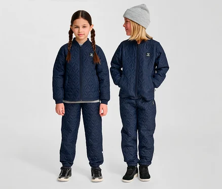 Zwei Kinder stehen in blauen, gesteppten hummel® »HMLSOBI Thermo-Sets« mit Jacke und Hose. Ein Kind trägt eine graue Mütze.
