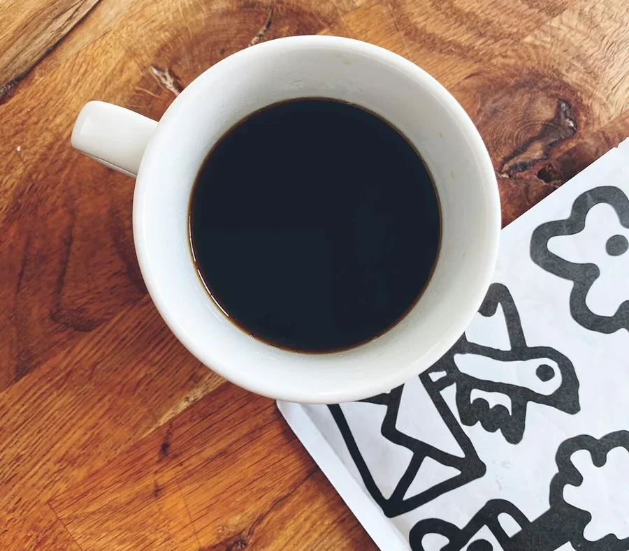 Draufsicht auf eine Tasse Kaffee neben einer weißen Serviette mit schwarzen Zeichnungen auf einem Holztisch.