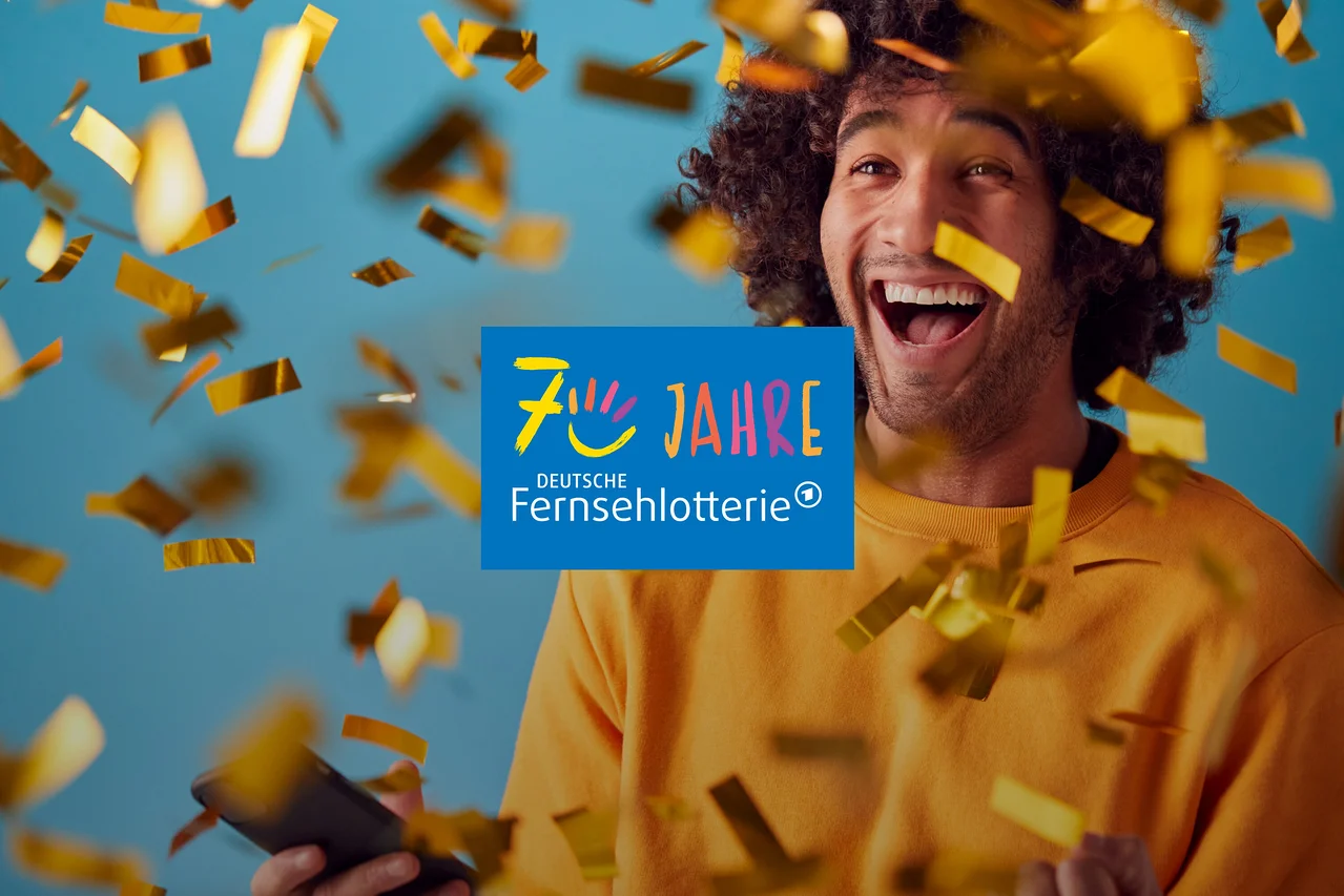 Ein lachender Mann mit lockigem Haar hält ein Smartphone, während goldener Konfetti um ihn herumfällt. In der Mitte ist das Logo „70 JAHRE DEUTSCHE FERNSEHLOTTERIE“ zu sehen.