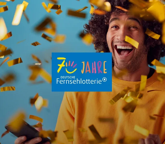 Ein lachender Mann mit lockigem Haar hält ein Smartphone, während goldener Konfetti um ihn herumfällt. In der Mitte ist das Logo „70 JAHRE DEUTSCHE FERNSEHLOTTERIE“ zu sehen.