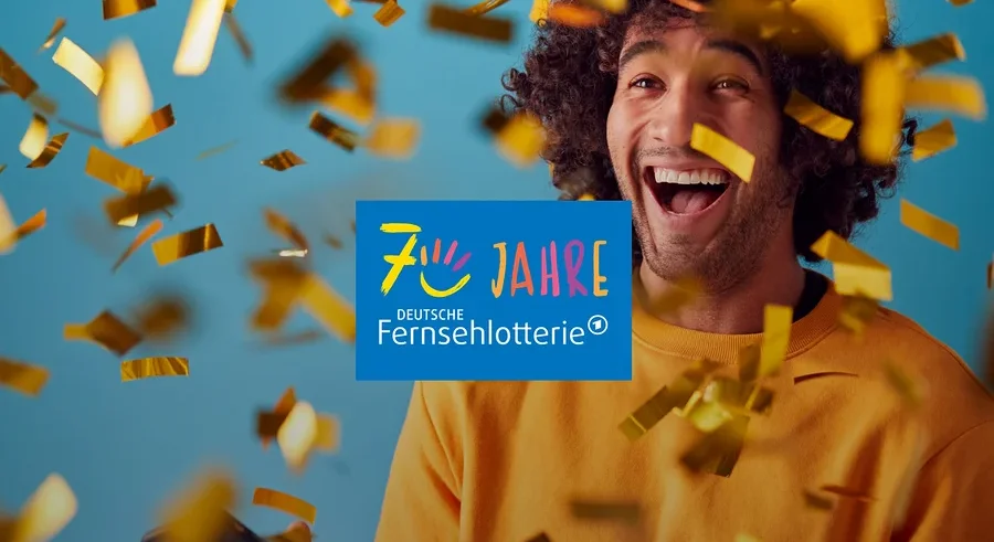 Ein lachender Mann mit lockigem Haar hält ein Smartphone, während goldener Konfetti um ihn herumfällt. In der Mitte ist das Logo „70 JAHRE DEUTSCHE FERNSEHLOTTERIE“ zu sehen.