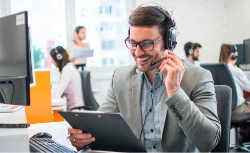 Mann mit Headset lächelt und hält Klemmbrett im Büro.