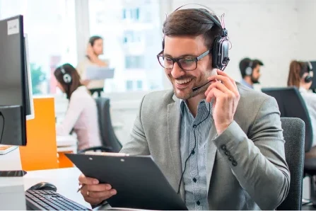 Mann mit Headset lächelt und hält Klemmbrett im Büro.