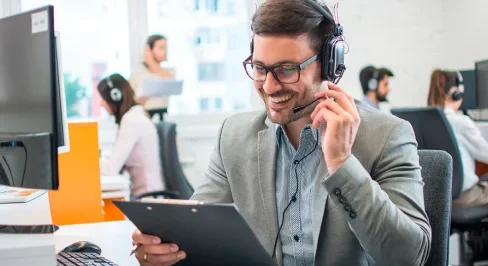 Mann mit Headset lächelt und hält Klemmbrett im Büro.