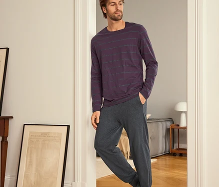 Mann lehnt an einer Tür, trägt ein lila gestreiftes Langarmshirt und graue Jogginghose.