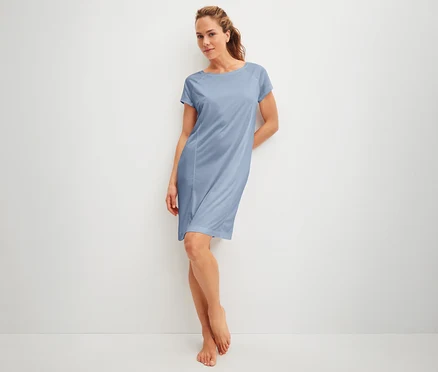 Frau lehnt an einer Wand und trägt ein blaues Kleid.