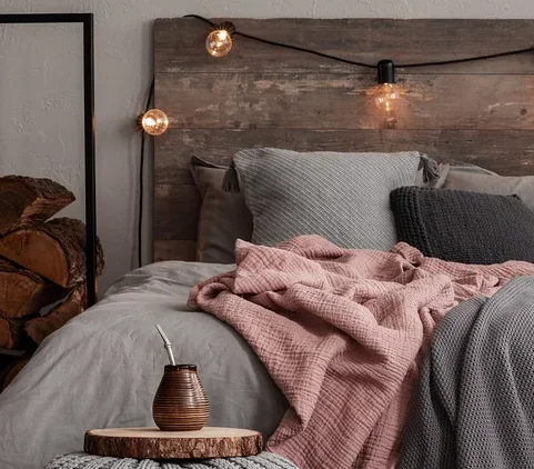 Ein Schlafzimmer mit einem Bett mit grauer Bettwäsche, einer rosa Decke und einer grauen Strickdecke. Auf dem Boden liegt ein gemusterter Teppich.