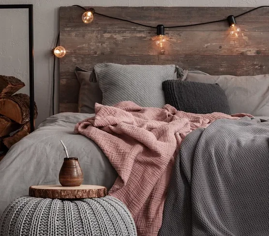 Ein Schlafzimmer mit einem Bett mit grauer Bettwäsche, einer rosa Decke und einer grauen Strickdecke. Auf dem Boden liegt ein gemusterter Teppich.