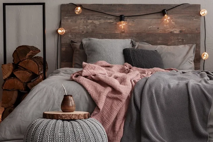 Ein Schlafzimmer mit einem Bett mit grauer Bettwäsche, einer rosa Decke und einer grauen Strickdecke. Auf dem Boden liegt ein gemusterter Teppich.
