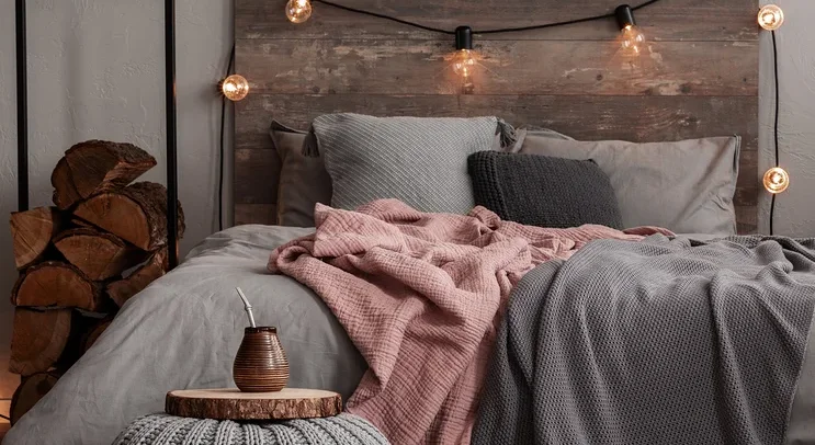 Ein Schlafzimmer mit einem Bett mit grauer Bettwäsche, einer rosa Decke und einer grauen Strickdecke. Auf dem Boden liegt ein gemusterter Teppich.