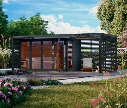 Moderne Außensauna mit Glasfront, verbunden mit einer Pergola mit Lamellenwänden, Liegestuhl und Beistelltisch in einem blühenden Garten.
