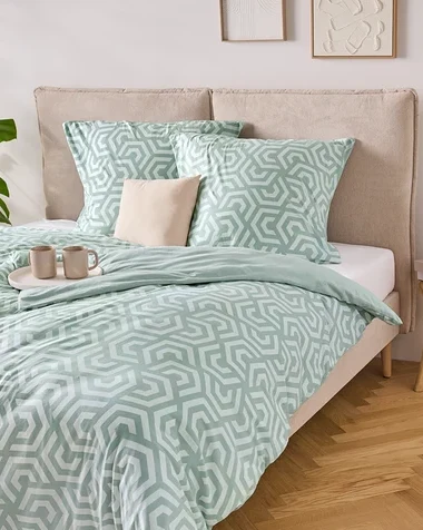 Ein Bett mit hellblau-weiß gestreifter Bettwäsche, zwei Kissen und einer Ablage mit zwei Tassen darauf.
