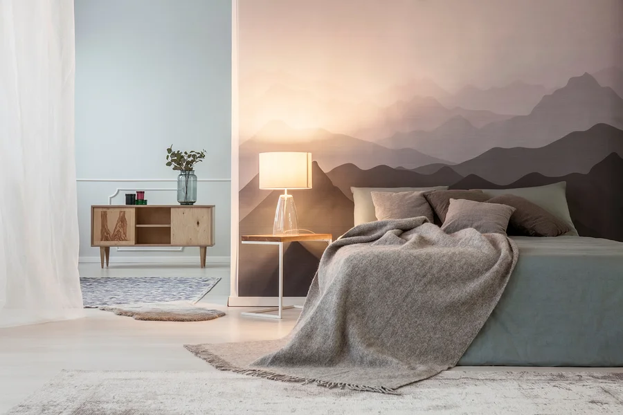 Ein Schlafzimmer mit einem Bett mit grauer Decke, einem Nachttisch mit Lampe und einer Kommode mit Dekoration.