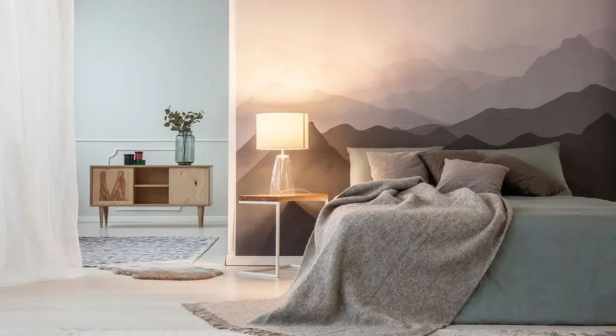 Ein Schlafzimmer mit einem Bett mit grauer Decke, einem Nachttisch mit Lampe und einer Kommode mit Dekoration.