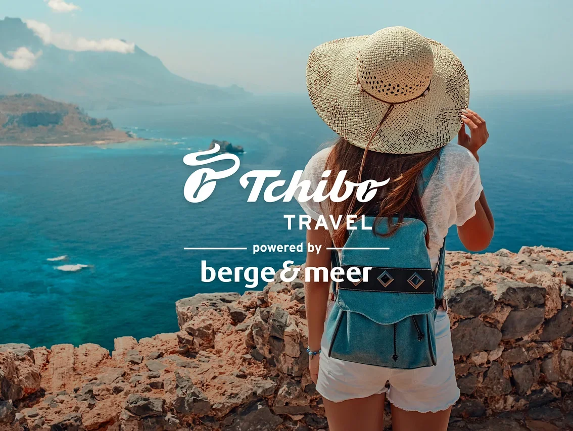 Frau mit Hut und blauem Rucksack steht auf Felsen mit Blick aufs Meer. Logos von Tchibo Travel und Berge&Meer.