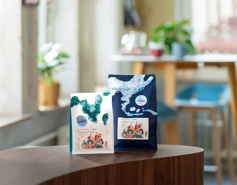Zwei Kaffeepackungen stehen auf einem Tisch, eine weiße und eine blaue.