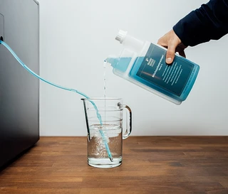 Person gießt flüssigen Reiniger in ein Glas, ein Schlauch führt zum Kaffeevollautomaten.