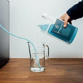 Person gießt flüssigen Reiniger in ein Glas, ein Schlauch führt zum Kaffeevollautomaten.