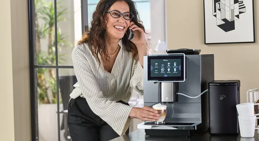 Frau hält ein Glas Kaffee an einer Kaffeemaschine und telefoniert.