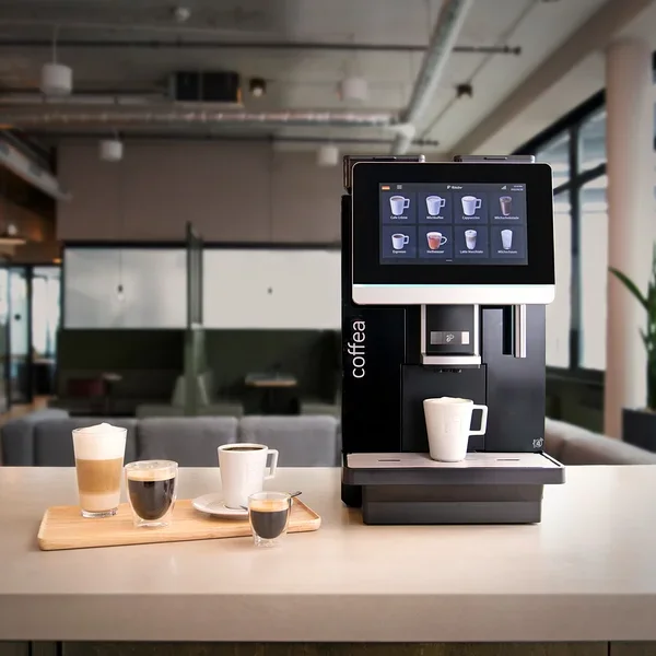 Vier Tassen Kaffee auf einem Holzbrett vor einer Kaffeemaschine in einem Büro.