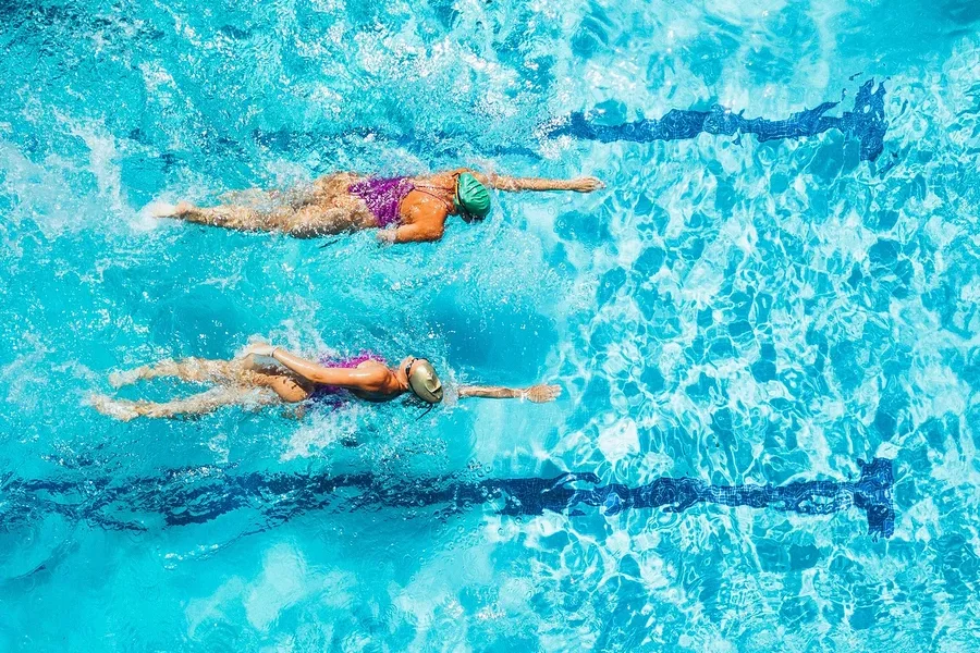Luftaufnahme von zwei Frauen, die in rosafarbenen Badeanzügen und Badekappen in einem Schwimmbad schwimmen.