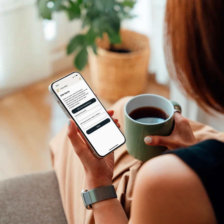 Frau hält eine Tasse Kaffee und schaut auf ihr Handy.