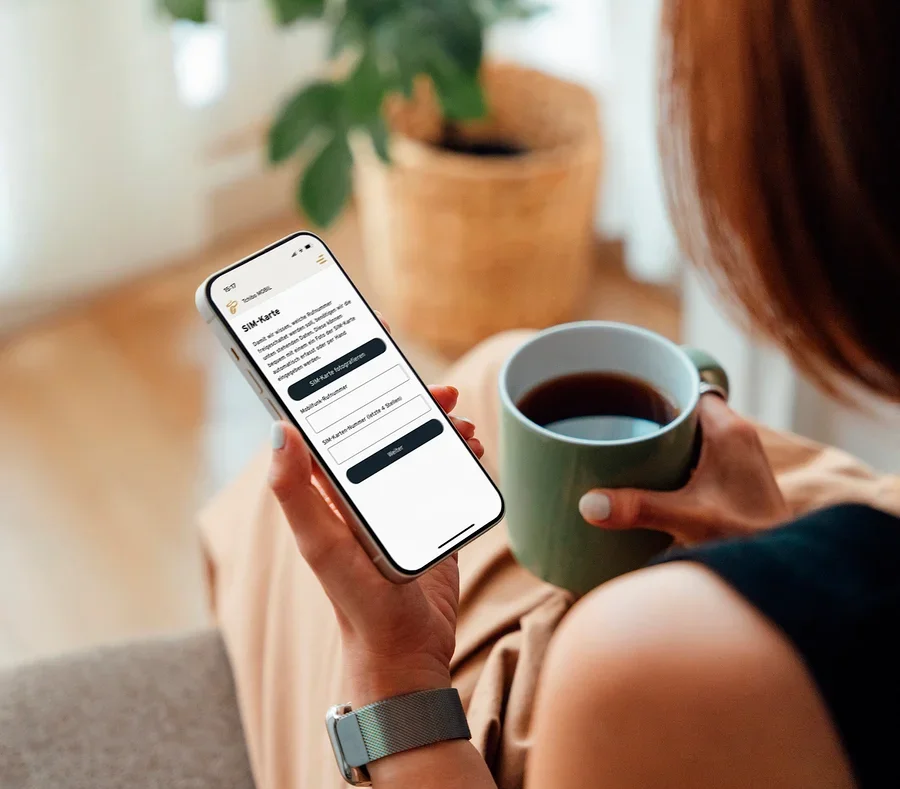 Frau hält eine Tasse Kaffee und schaut auf ihr Handy.
