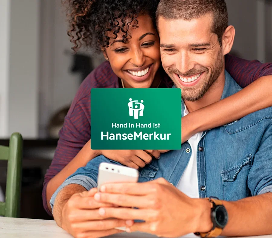 Ein lächelndes Paar schaut auf ein Mobiltelefon. Die Frau umarmt den Mann um die Schultern.