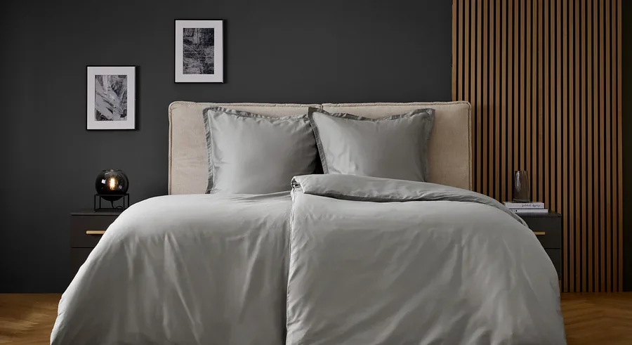 Graue Bettwäsche auf einem Bett mit zwei Kissen und Nachttischen an den Seiten.