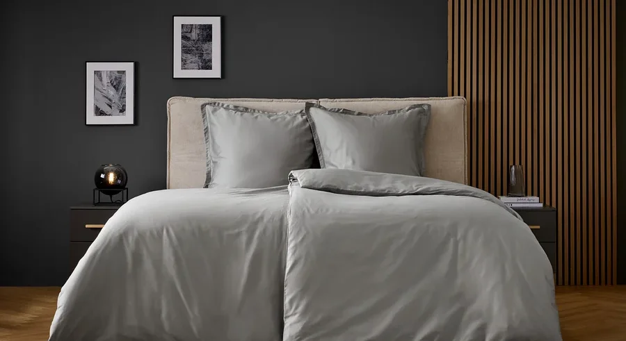 Graue Bettwäsche auf einem Bett mit zwei Kissen und Nachttischen an den Seiten.