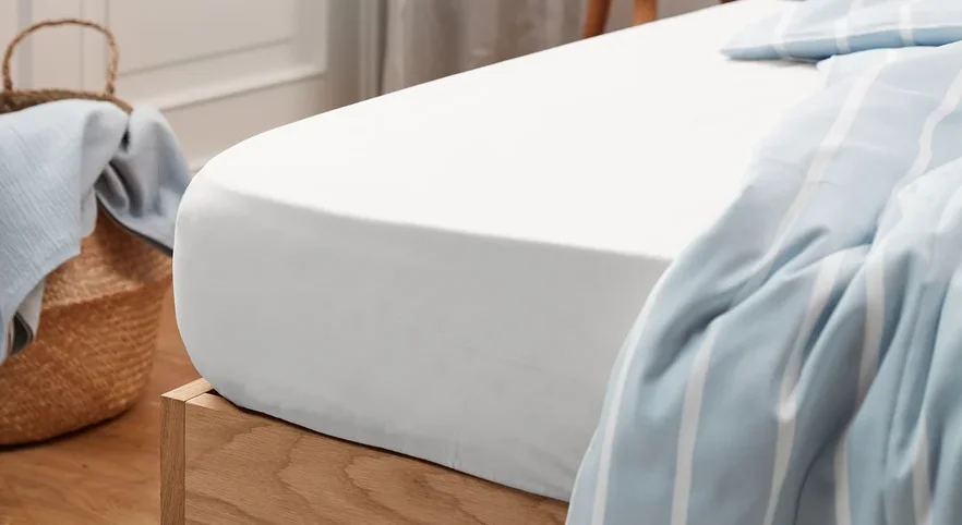 Weißes Perkal-Spannbettlaken in Standardgröße auf einem Bett mit Holzrahmen.