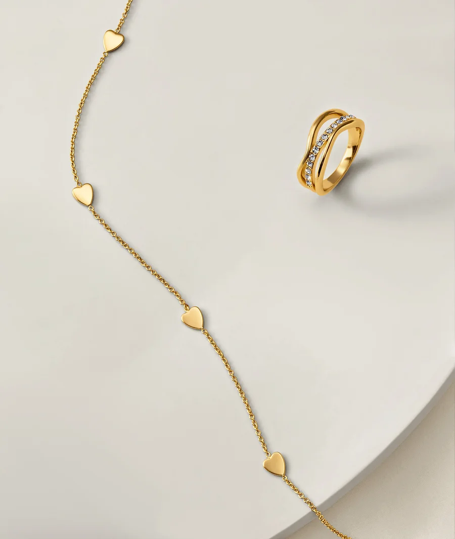 Goldene Kette mit Herzanhängern und goldener Ring mit Steinen auf weißem Hintergrund.