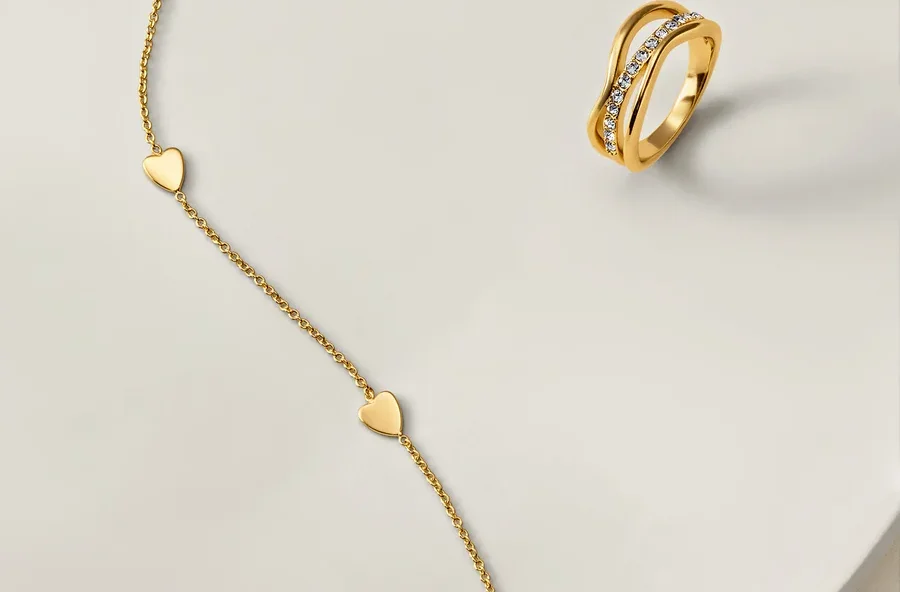 Goldene Kette mit Herzanhängern und goldener Ring mit Steinen auf weißem Hintergrund.
