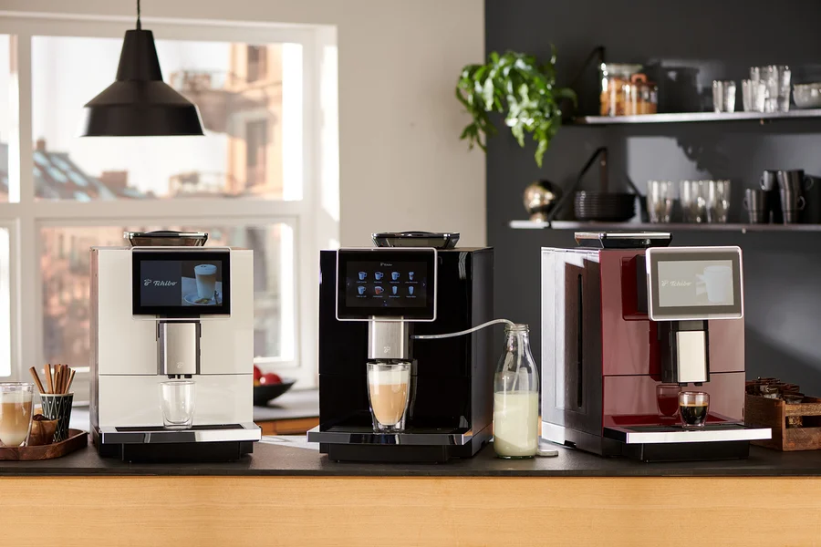 Drei Tchibo Office Kaffeevollautomaten in Weiß, Schwarz und Rot stehen nebeneinander auf einer Küchentheke und bereiten Kaffee zu.