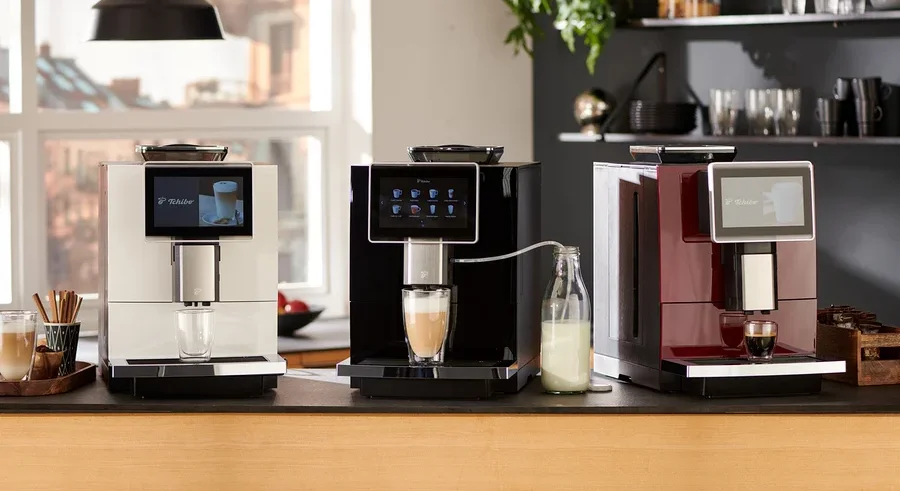 Drei Tchibo Office Kaffeevollautomaten in Weiß, Schwarz und Rot stehen nebeneinander auf einer Küchentheke und bereiten Kaffee zu.