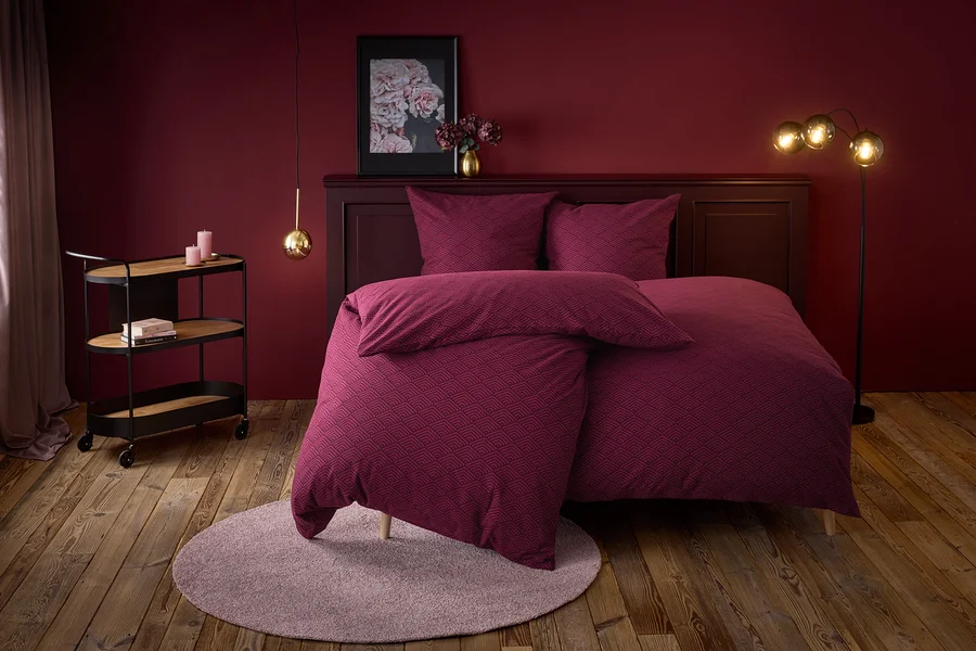 Weinrotes Schlafzimmer mit einem Bett mit geometrischem Muster, einem runden Teppich und einem Servierwagen.