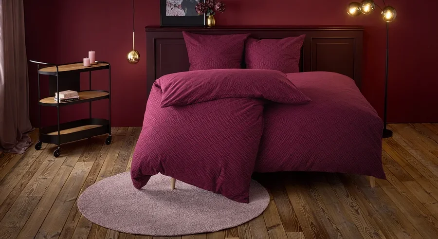 Weinrotes Schlafzimmer mit einem Bett mit geometrischem Muster, einem runden Teppich und einem Servierwagen.