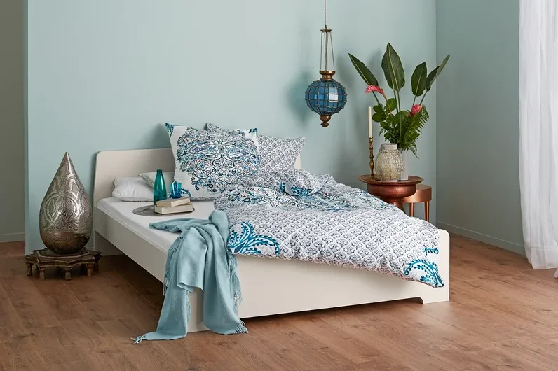 Schlafzimmer mit einem Bett mit blau-weißer Bettwäsche, Lampe und dekorativen Elementen.