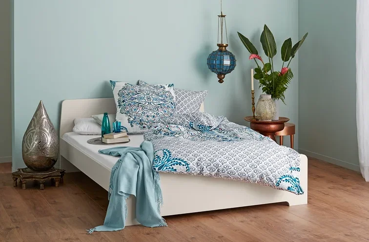 Schlafzimmer mit einem Bett mit blau-weißer Bettwäsche, Lampe und dekorativen Elementen.